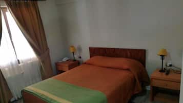 A single-bed room with a wooden headboard, two bedside tables with lamps, and a window with curtains.