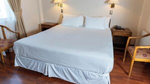 Una cama bien hecha con sábanas blancas, dos lámparas de noche y una mesita de madera con un teléfono.