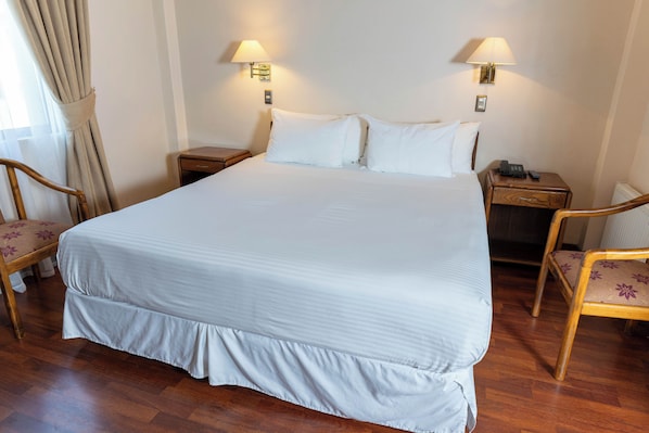 A neatly made bed with white linens, two bedside lamps, and a wooden nightstand with a phone. - Hotel Francisco de Aguirre Serena (La Serena)