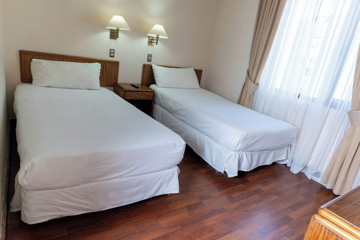 Una habitación de hotel con dos camas individuales, cabeceros de madera, mesitas de noche y lámparas.