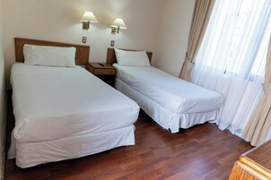 Una habitación de hotel con dos camas individuales, cabeceros de madera, mesitas de noche y lámparas.