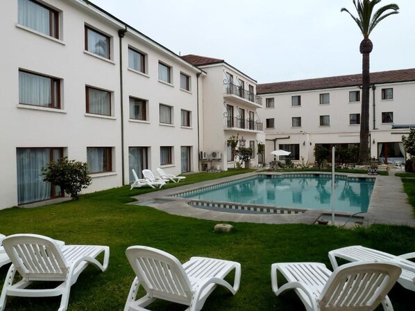 A courtyard with a swimming pool, white lounge chairs, and a palm tree.