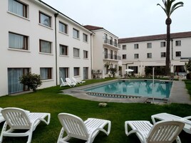 Un patio con piscina, sillas de descanso blancas y una palmera.