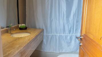 A bathroom with a wooden vanity, a white sink, a mirror, a toilet, and a shower curtain.