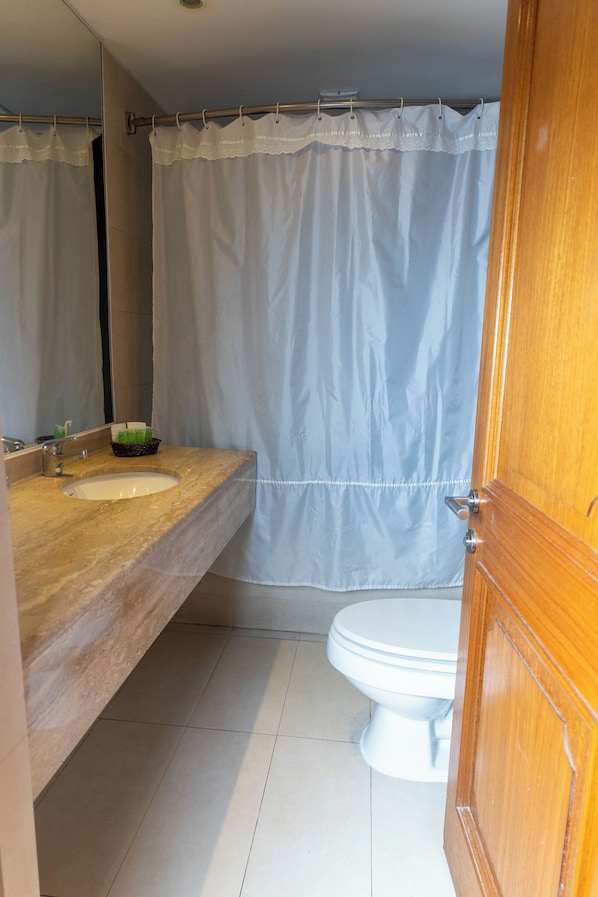 Un baño con tocador de madera, un lavamanos blanco, un espejo, un inodoro y una cortina de ducha.