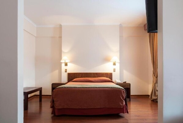Habitación de hotel con una cama individual, dos mesitas de noche, un banco y un televisor instalado en la pared.