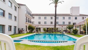 Un patio de hotel con piscina, edificios blancos y una palmera.