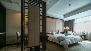 A hotel room with a large bed, a chair, a desk, and a decorative screen.