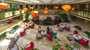 A spacious indoor area with multiple seating arrangements, including round tables and chairs, surrounded by potted plants.