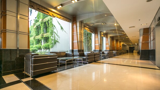 A modern lobby with a long reception desk, seating area, and large windows with greenery.