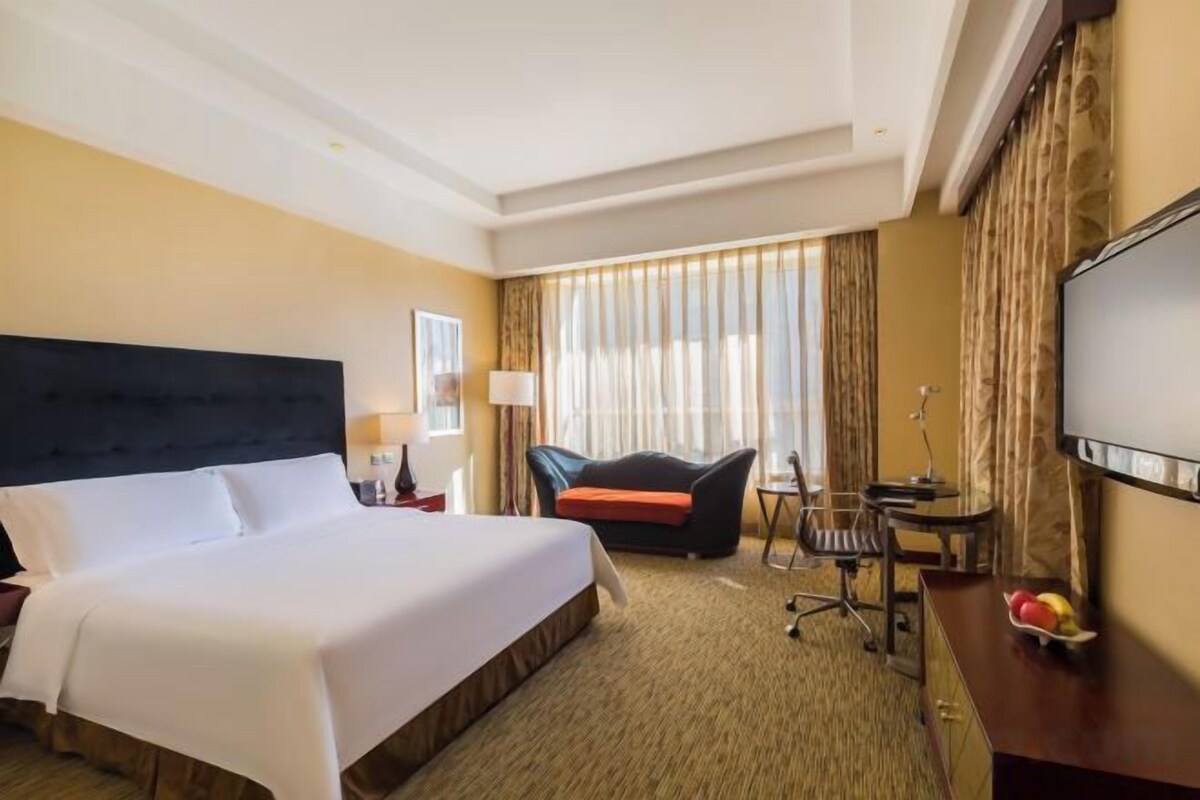 Una habitación de hotel con una cama grande, un escritorio con una silla, un televisor y una ventana con cortinas.