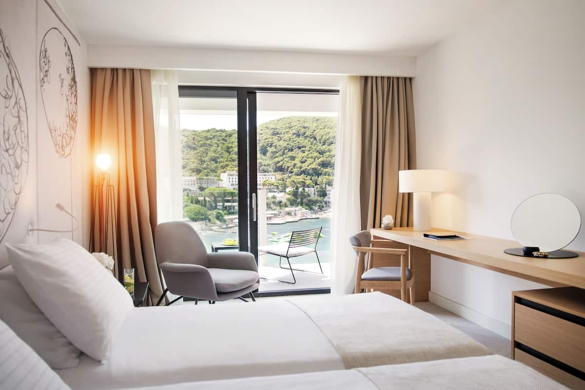 Habitación de hotel con cama, escritorio, silla y vistas a un lago y montañas.