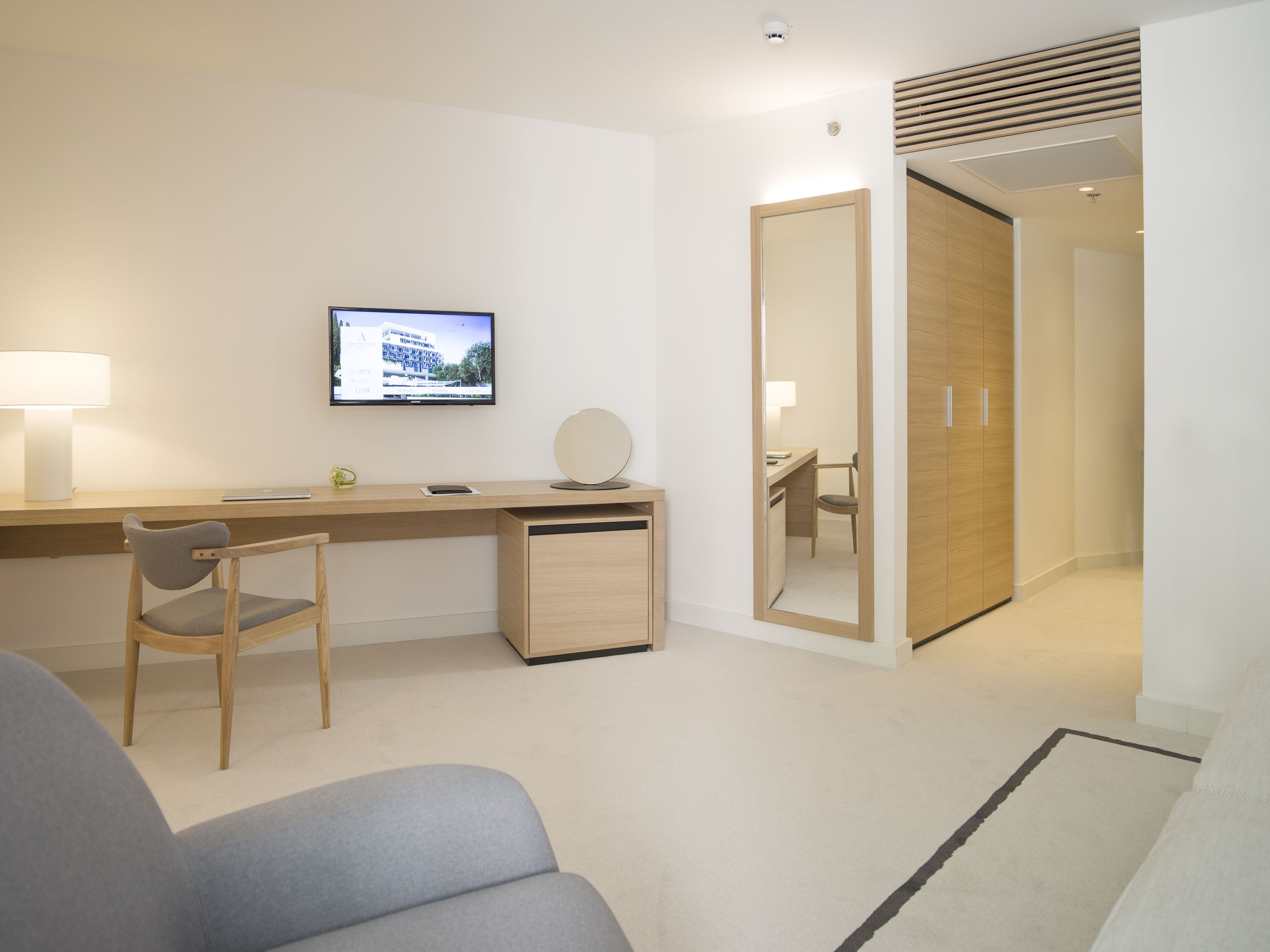 Une chambre d’hôtel moderne équipée d’un bureau, d’une chaise et d’un téléviseur qui diffuse une image d’un bâtiment.