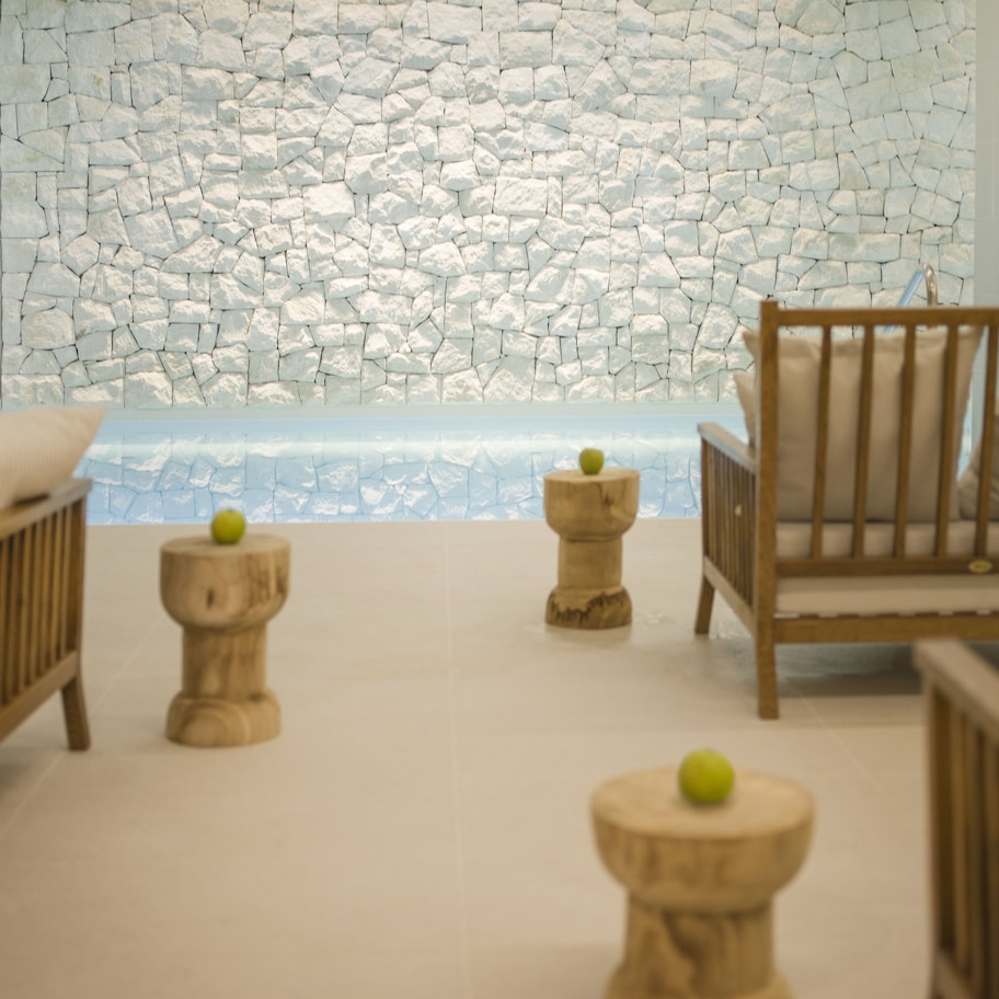 A room with a stone wall, a wooden crib, a wooden chair, and a small wooden stool with an apple on it.