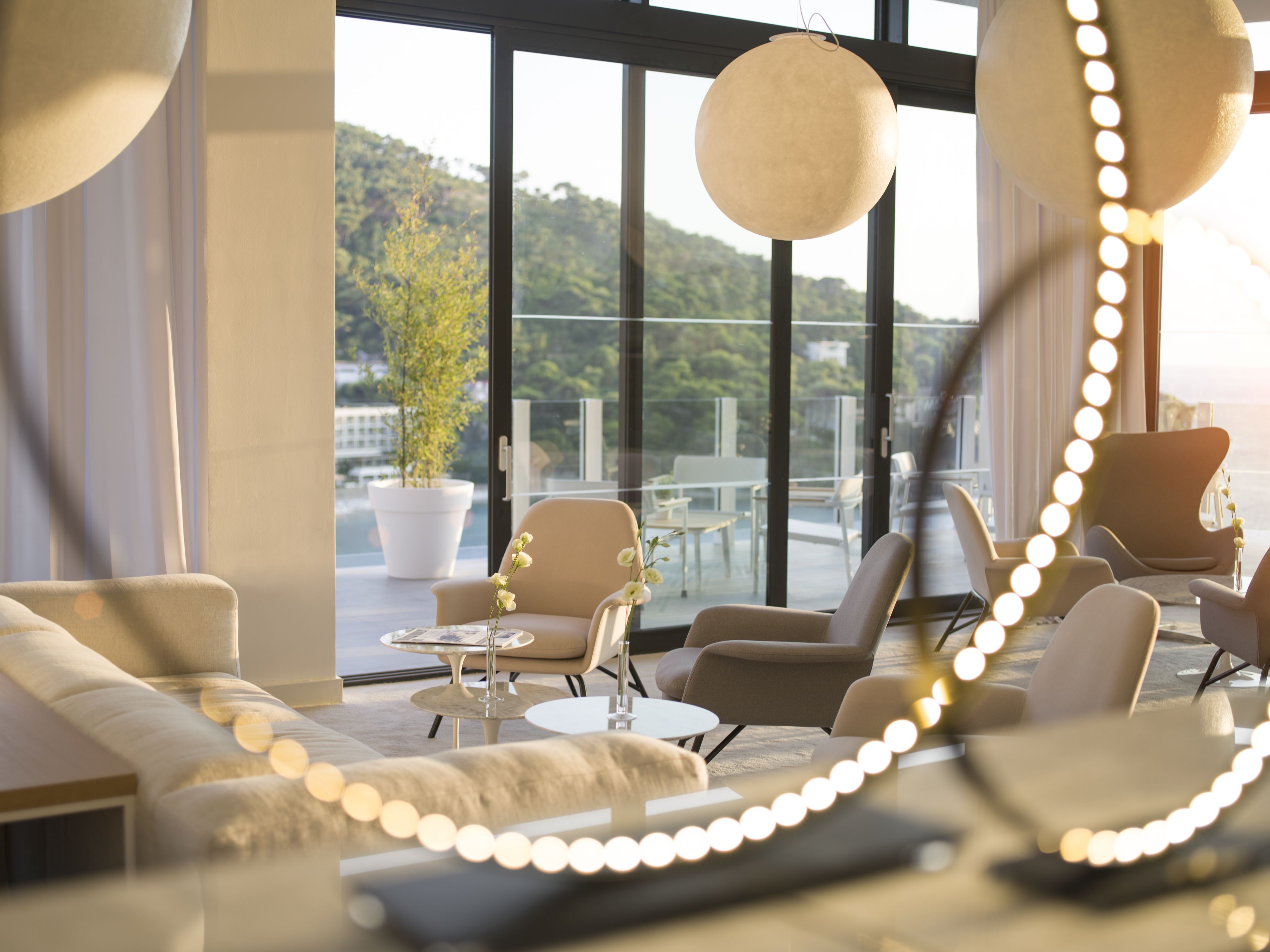 Eine moderne Lounge mit Sofas, Sesseln und einem großen Fenster mit Blick auf eine grüne Landschaft.