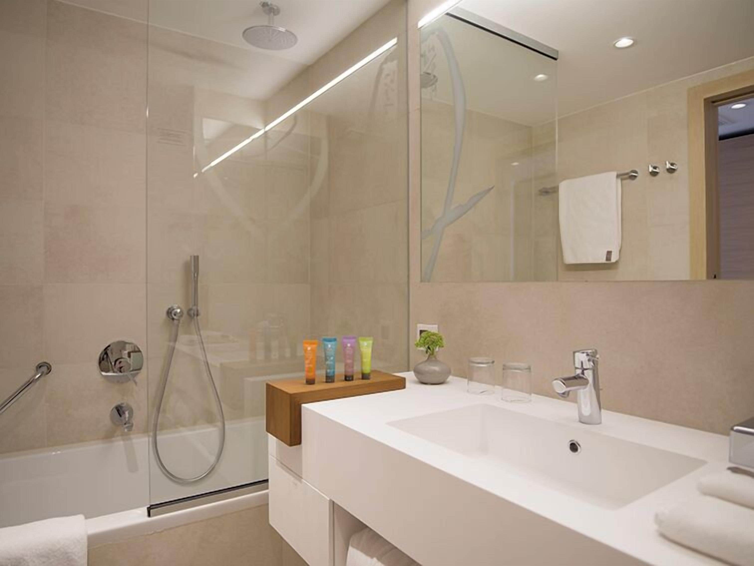 A modern bathroom with a glass-enclosed shower, a white sink, and a mirror above it.