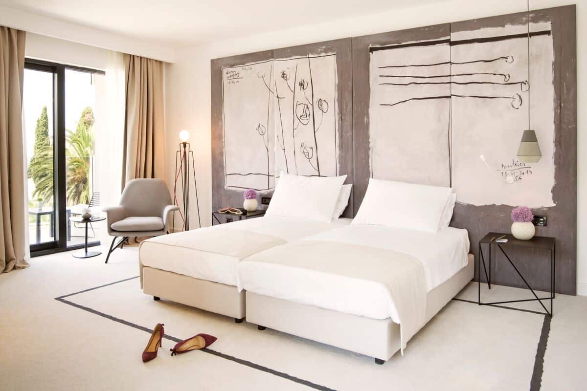 Habitación de hotel moderna con una cama grande, una silla, una mesita de noche y vistas al exterior.