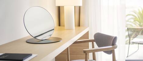 A modern, minimalist desk with a round mirror, a lamp, and a chair.