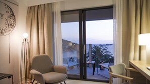 A hotel room with a large sliding glass door leading to a balcony with a view of the sea and palm trees. There are two chairs and a small table on the balcony. - Hotel Kompas (Dubrovnik)