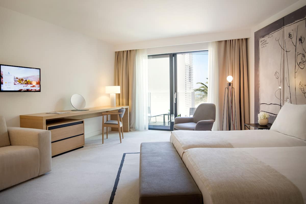 Habitación de hotel con cama, escritorio, silla, televisión y un amplio ventanal con cortinas.