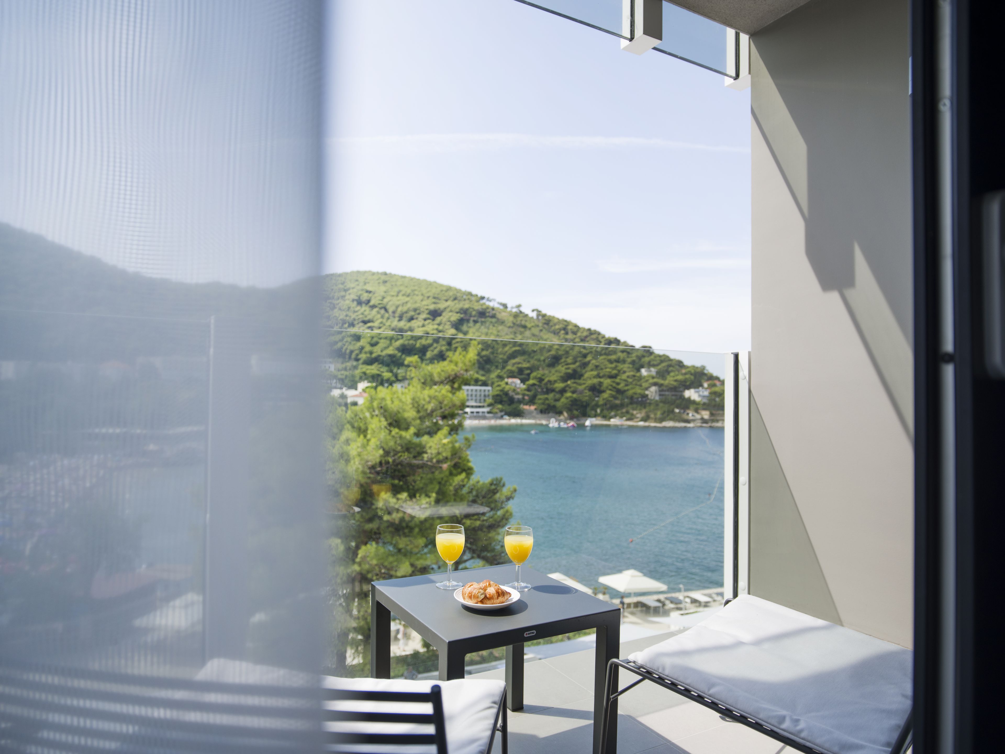 A balcony with a table, a chair, and a view of a body of water and a hill.