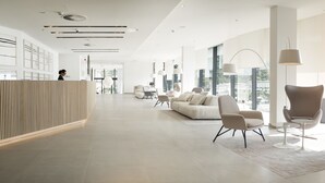 A spacious lobby with a reception desk, modern seating, large windows, and a view of the city. - Hotel Kompas (Dubrovnik)