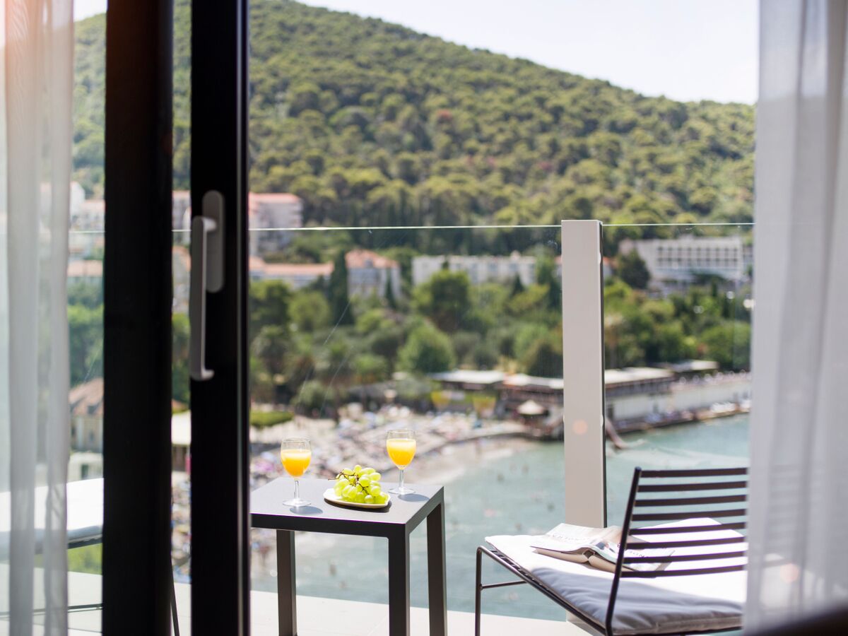 Un balcon avec une table dressée pour deux personnes, offrant une vue panoramique sur une rivière et un paysage vallonné.