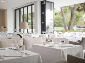 A restaurant with tables set for dining, large windows, and a view of trees.