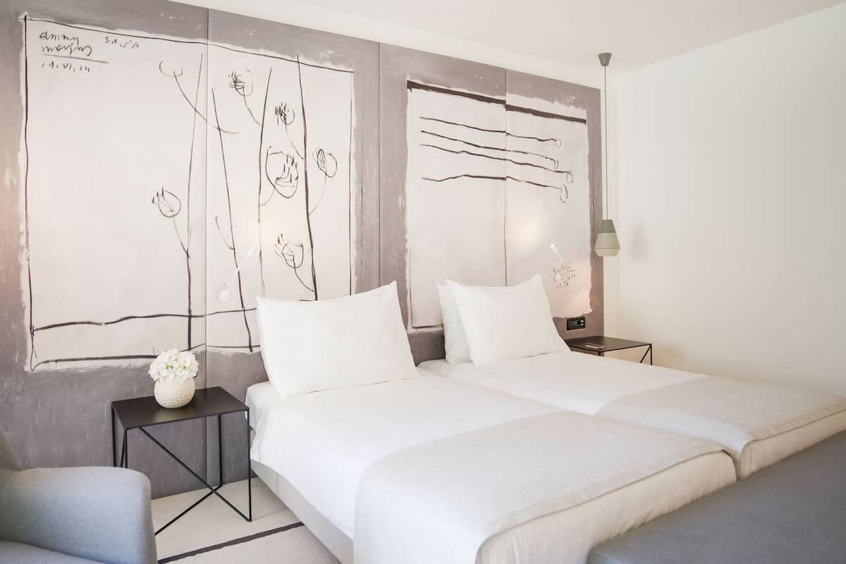 Un dormitorio con dos camas, una mesita con un florero y una pared decorada con dibujos abstractos.