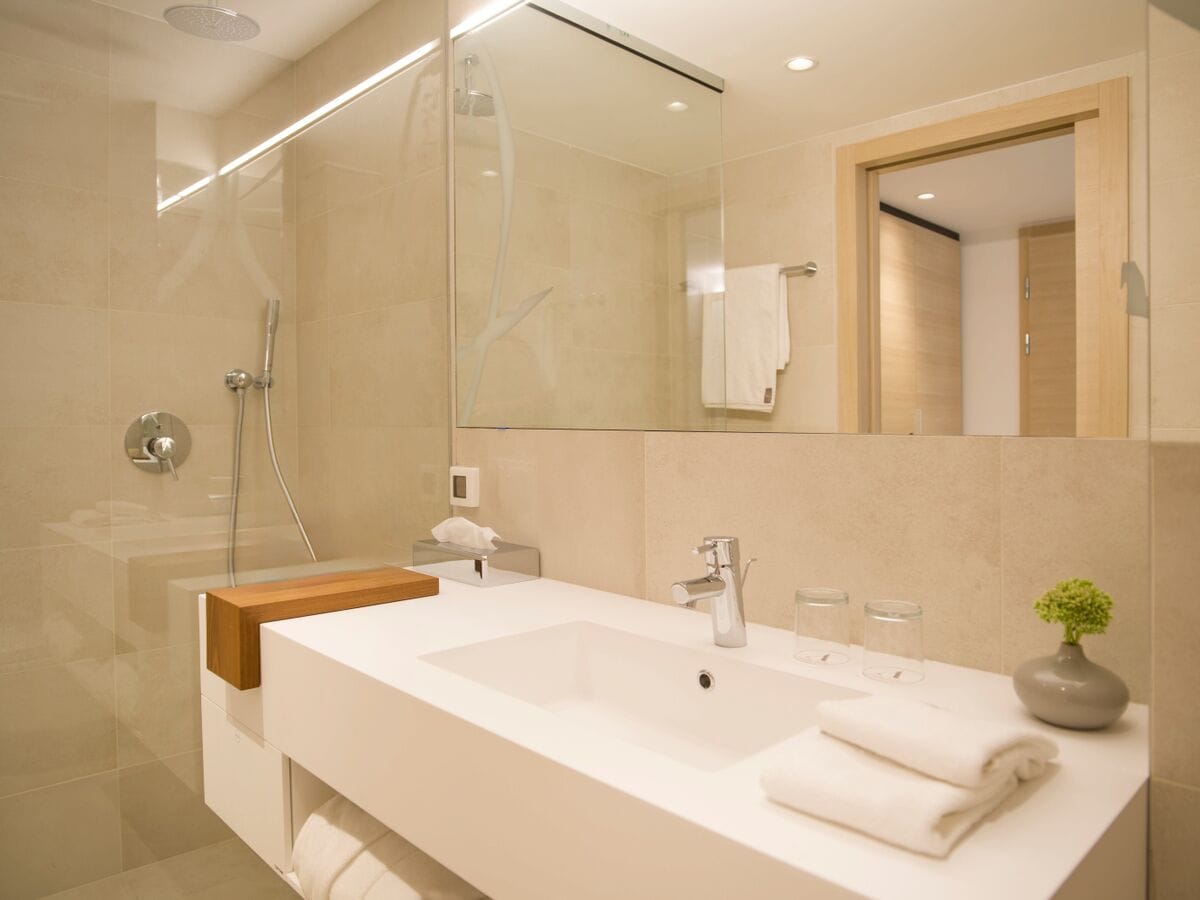 Un bany modern amb un mirall gran, un lavabo blanc, un box de dutxa de vidre i una petita planta a la superfície.