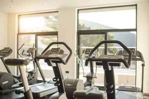 Un gimnasio con cintas de correr y equipo de ejercicio, amplias ventanas con vistas a montañas y un interior luminoso.
