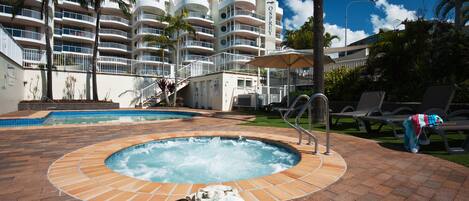 A hotel pool area with a hot tub, lounge chairs, and palm trees.