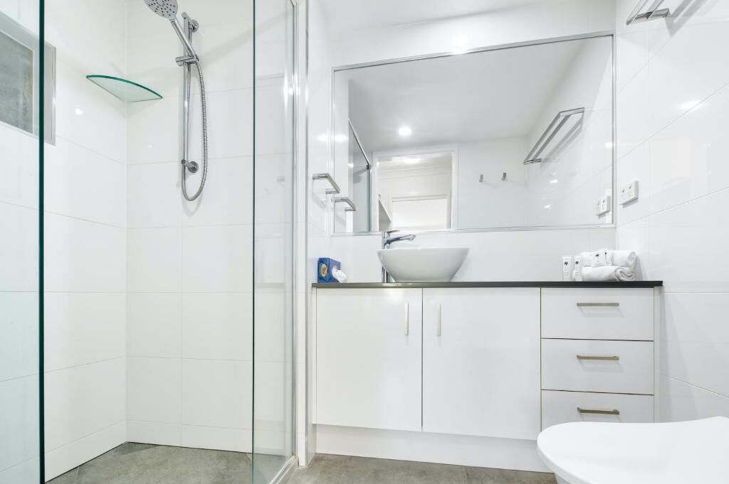 A modern bathroom with a glass shower enclosure, a white sink, and a large mirror.