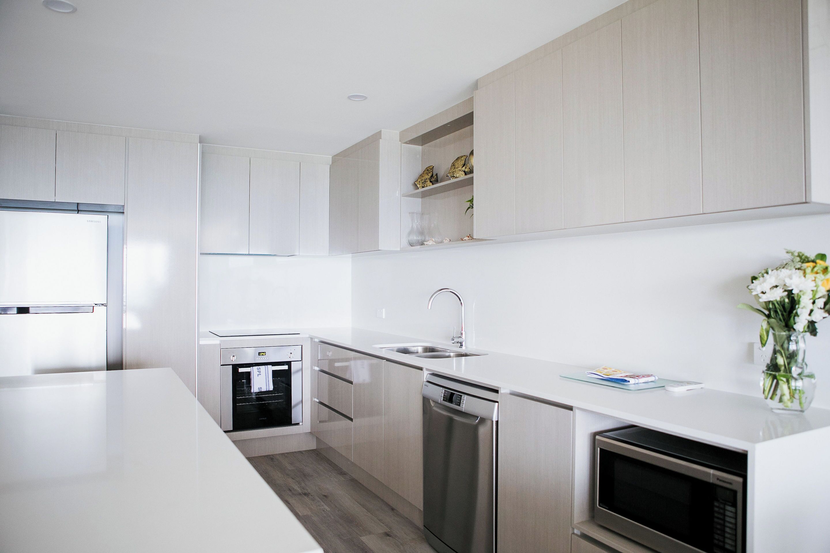 A modern kitchen with white cabinetry, stainless steel appliances, and a built-in oven.