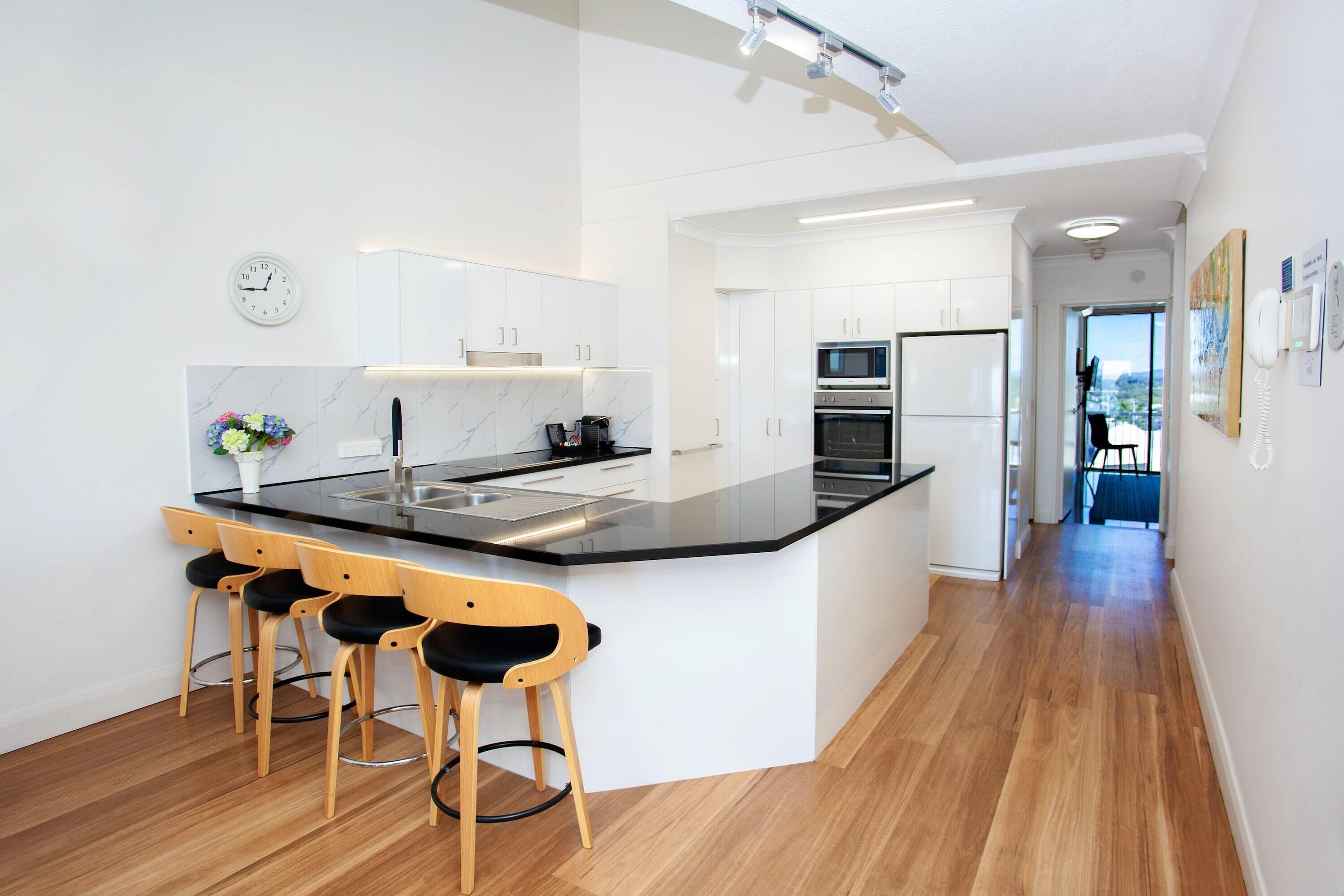 A modern kitchen with a central island, bar stools, and a clock on the wall.