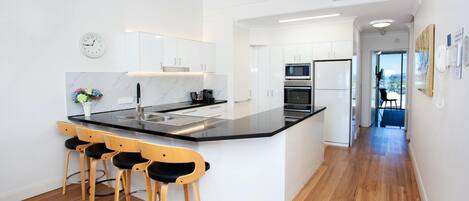 A modern kitchen with a central island, bar stools, and a clock on the wall.