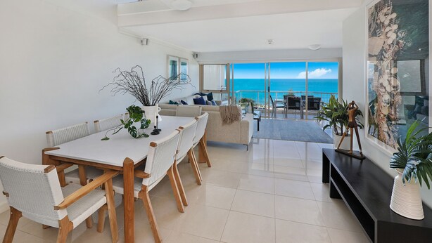 A modern living room with a dining area, large windows, and a view of the ocean. - Osprey Apartments (Mooloolaba)