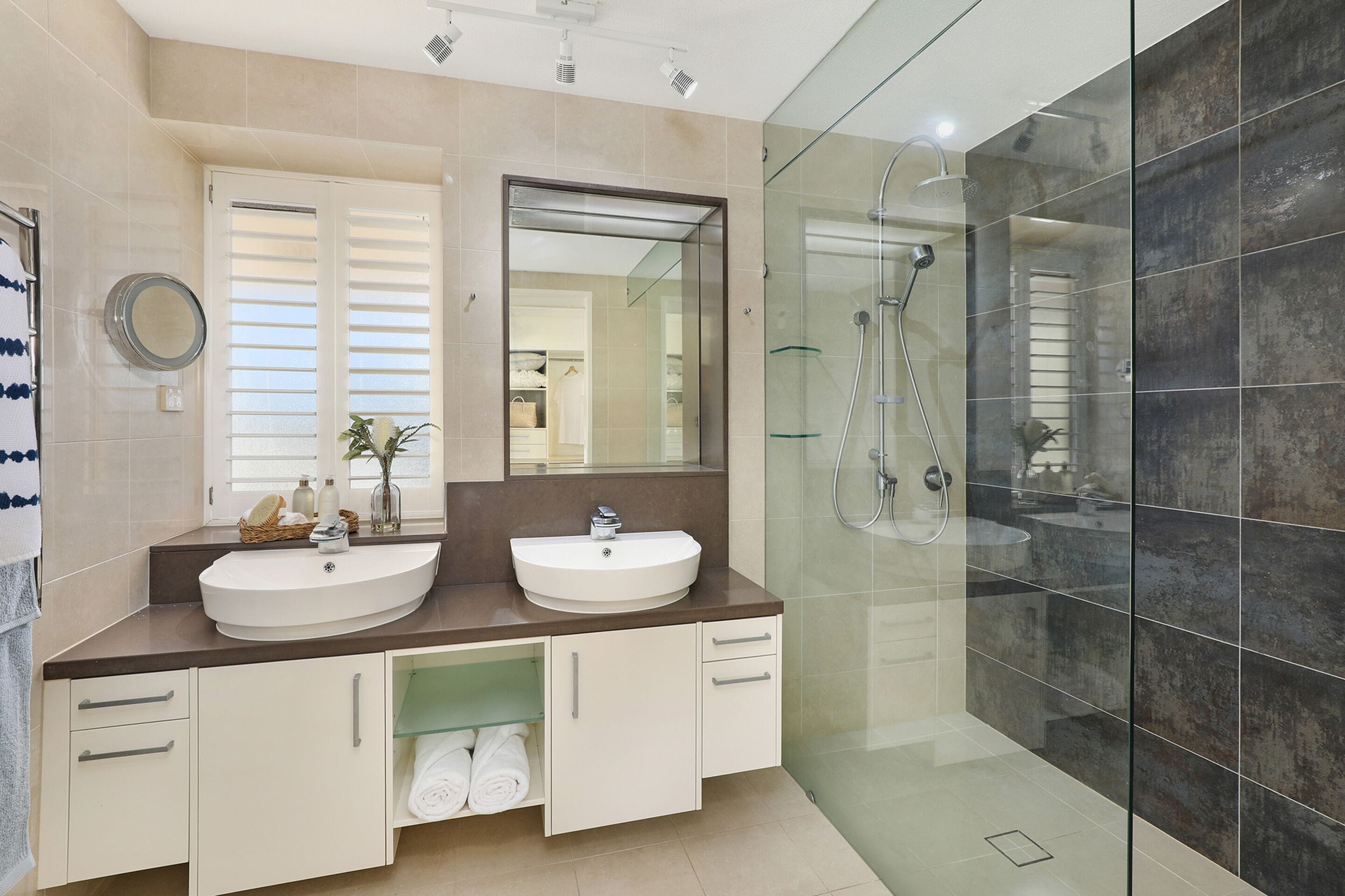 A modern bathroom with two sinks, a large mirror, and a glass-enclosed shower area.