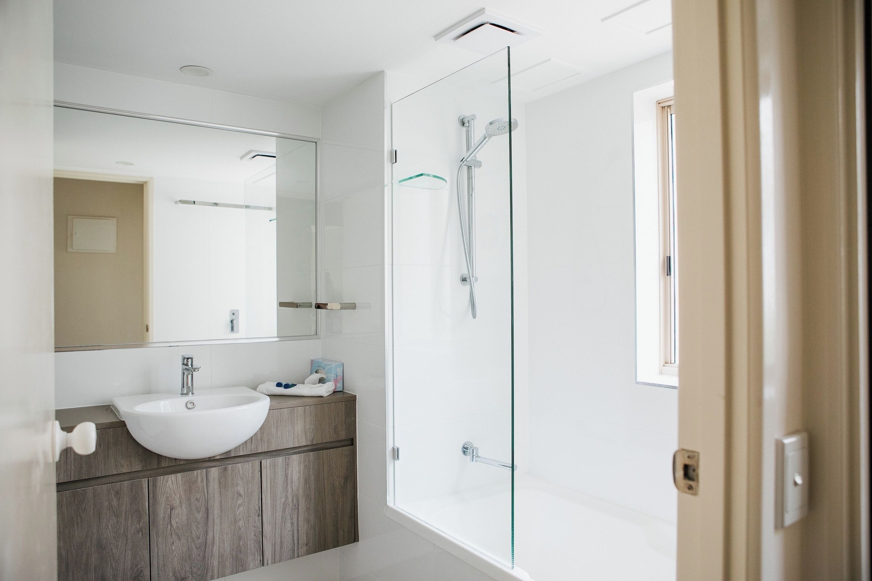 Un bagno moderno con cabina doccia in vetro, lavandino bianco e mobile bagno in legno.
