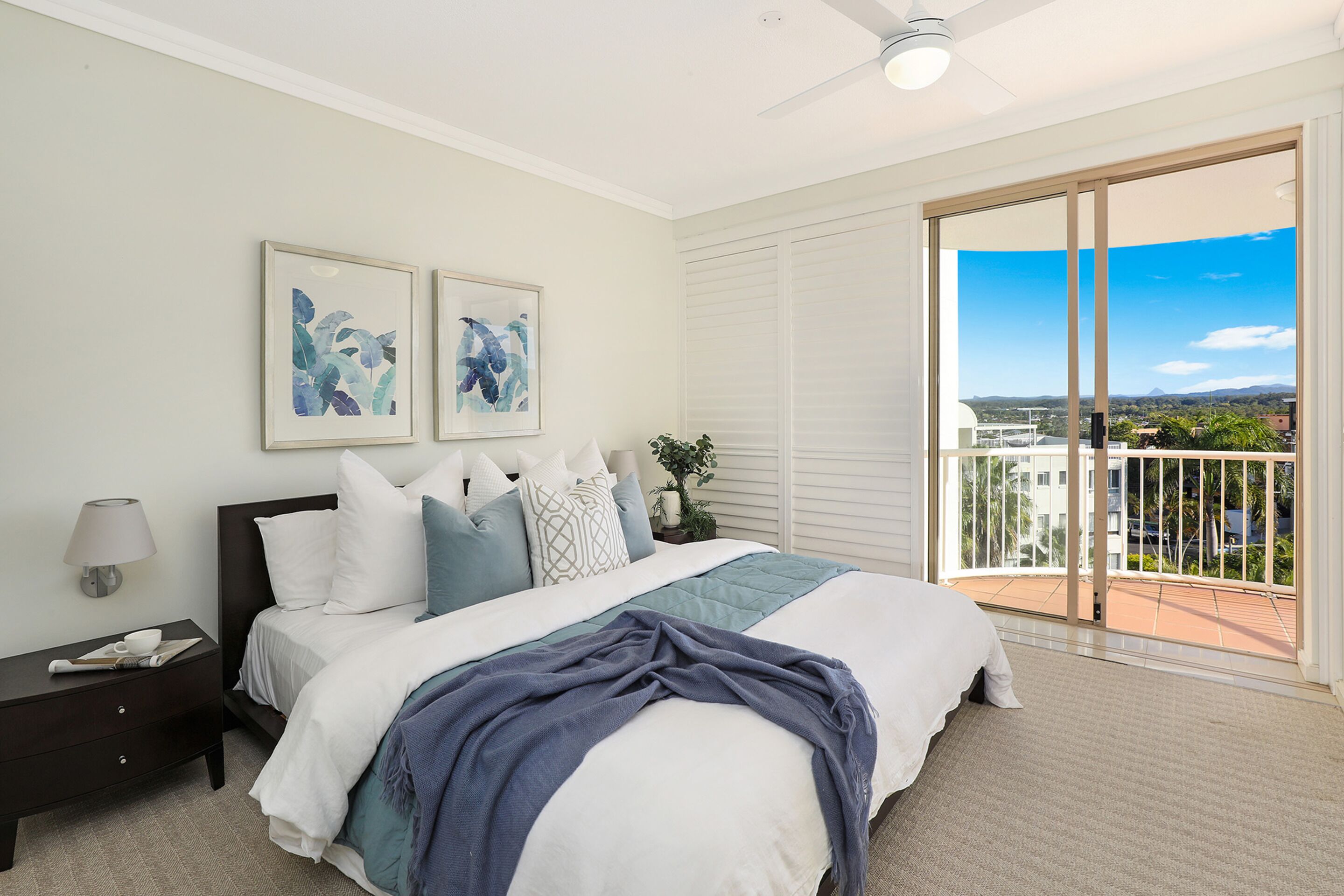 A bedroom with a bed, a nightstand, a lamp, and a view of the outside through a sliding door.