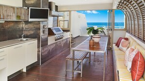 A modern kitchen with a built-in oven and microwave, a dining area with a wooden table and chairs, and a sofa with cushions. - Osprey Apartments (Mooloolaba)