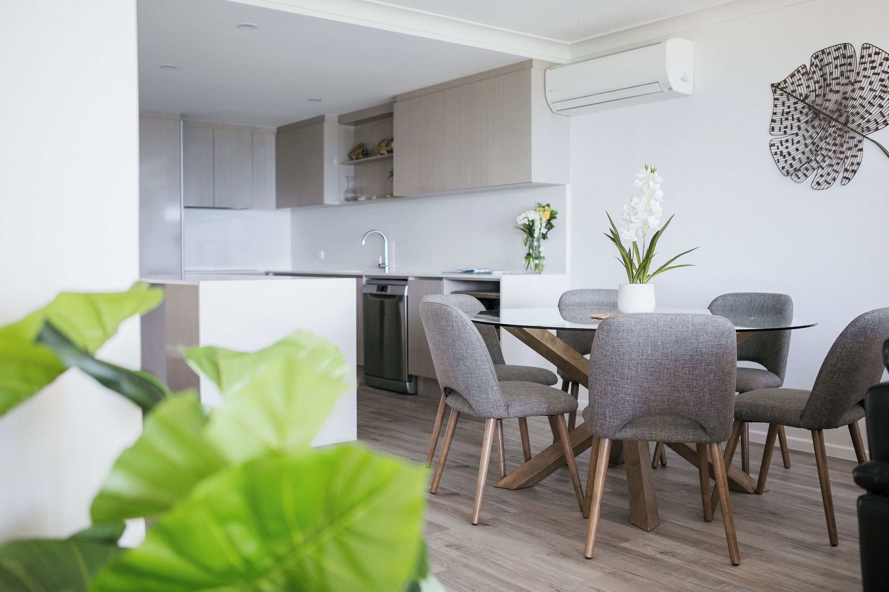 Une cuisine moderne avec des meubles gris, un évier en acier inoxydable et un coin repas comprenant des chaises grises à revêtement et une table en bois.