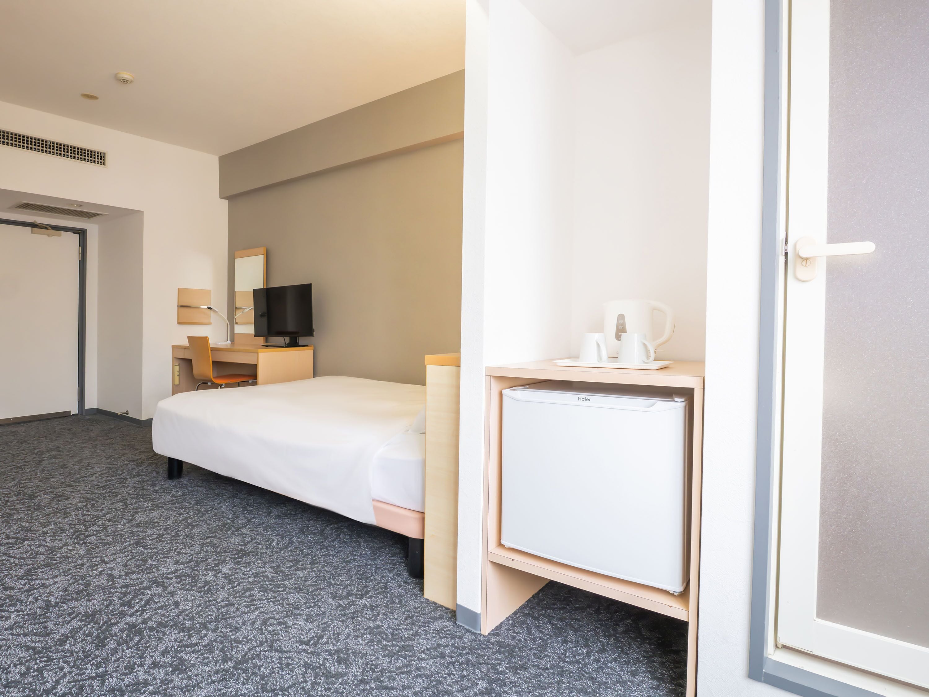 A hotel room with a bed, a desk with a computer, a television, a coffee maker, and a mini-fridge.