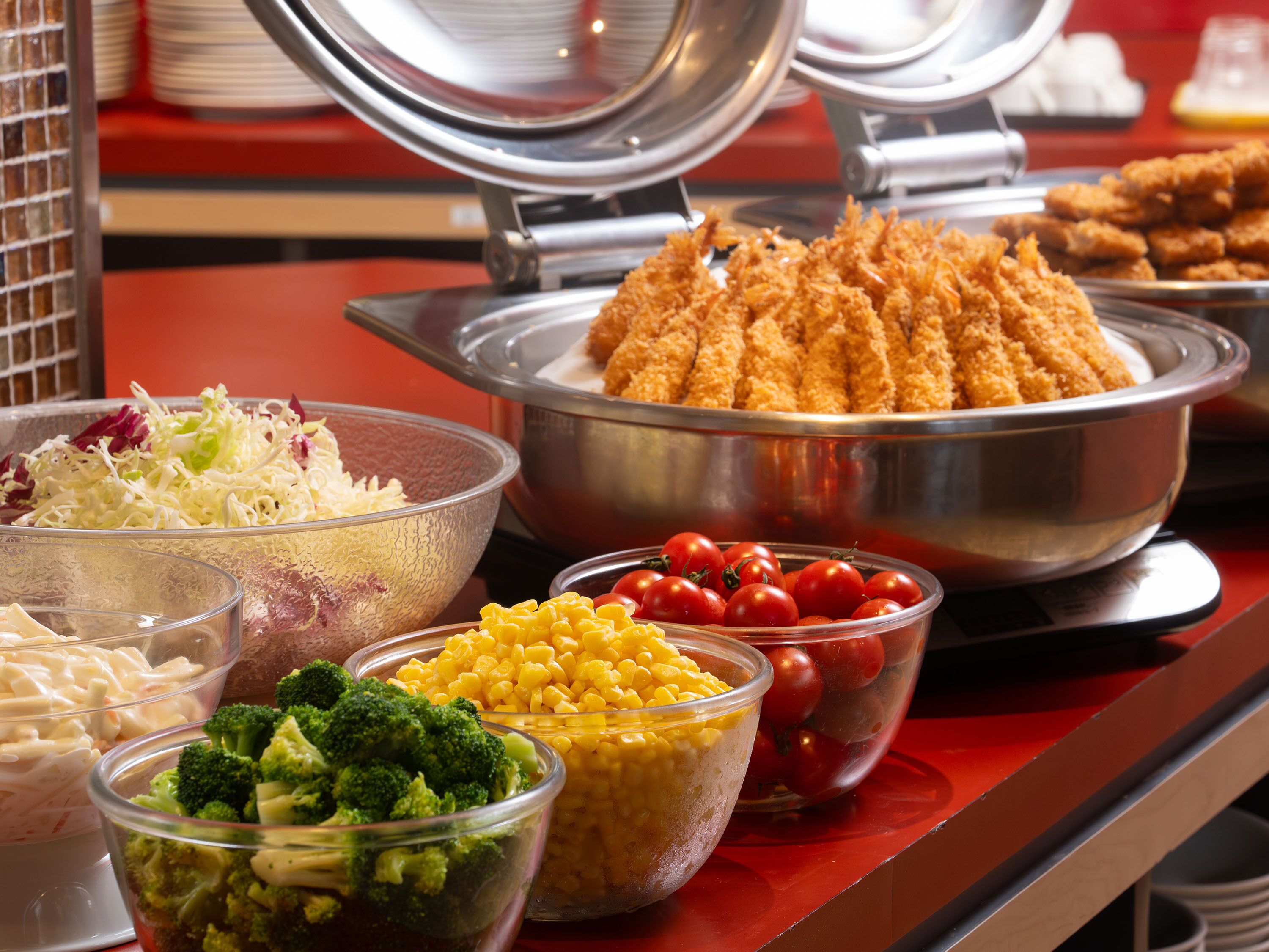 A buffet with various food items including salads, corn, broccoli, and fried items.