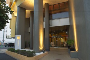 Ingresso moderno di un hotel con ampie colonne, una facciata ben illuminata e un cartello visibile.