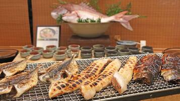 A variety of grilled fish and seafood on a grill, with small bowls of sauces in the background.