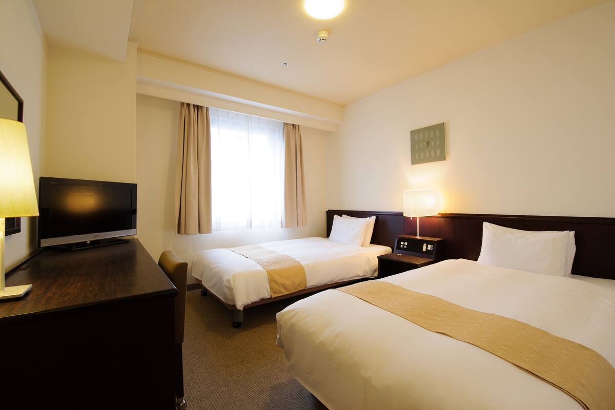 Habitación de hotel con dos camas, televisión y mesita de noche con lámpara.