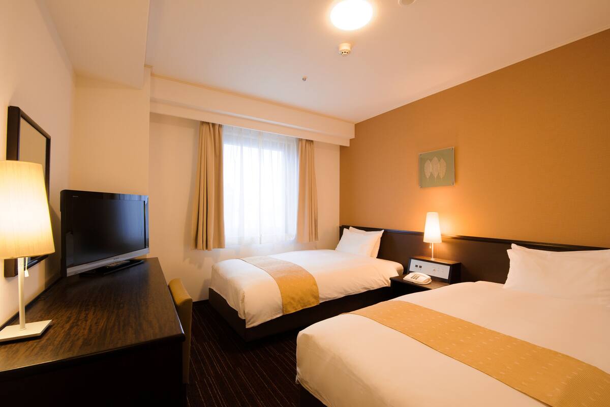Habitación de hotel con dos camas, televisión, escritorio con lámpara y mesita de noche con teléfono.