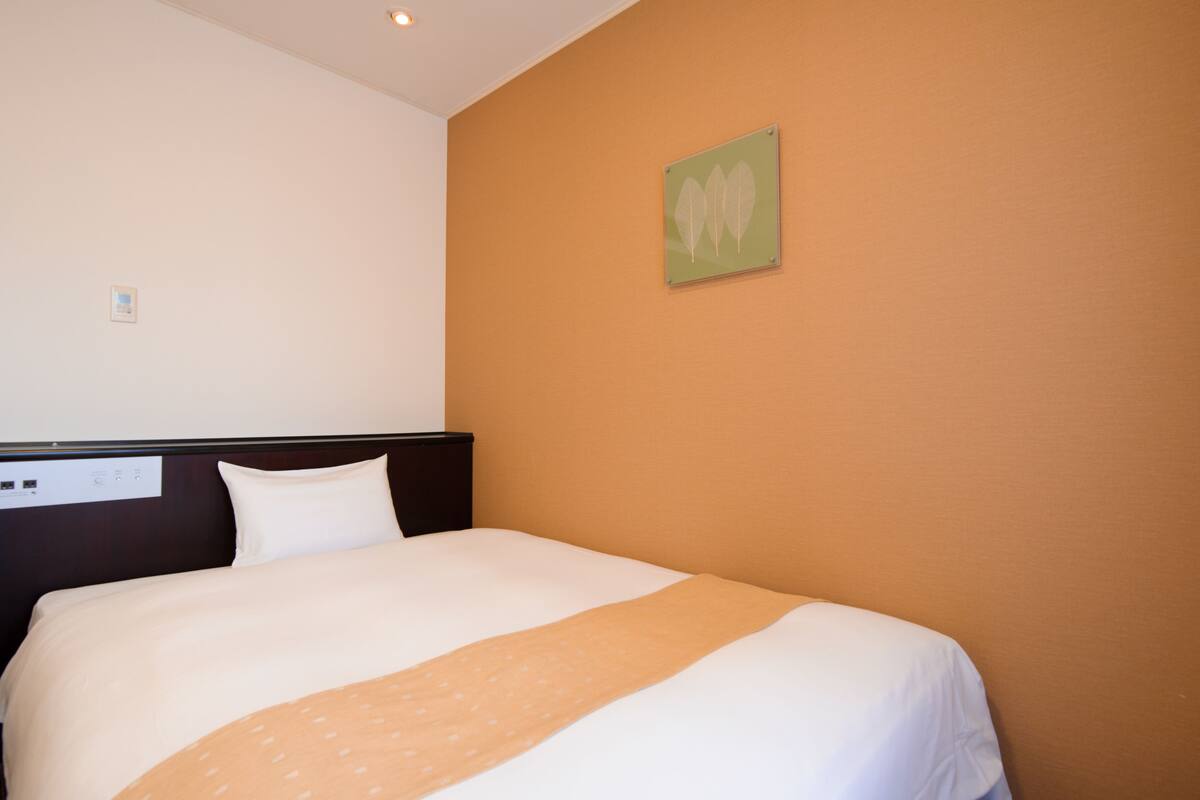 Habitación de hotel con cama, cabecera, panel de control en la pared y un cuadro enmarcado.