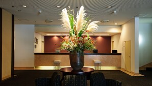 Un área de recepción con un jarrón grande de flores, un mostrador de recepción y asientos con un diseño estampado.